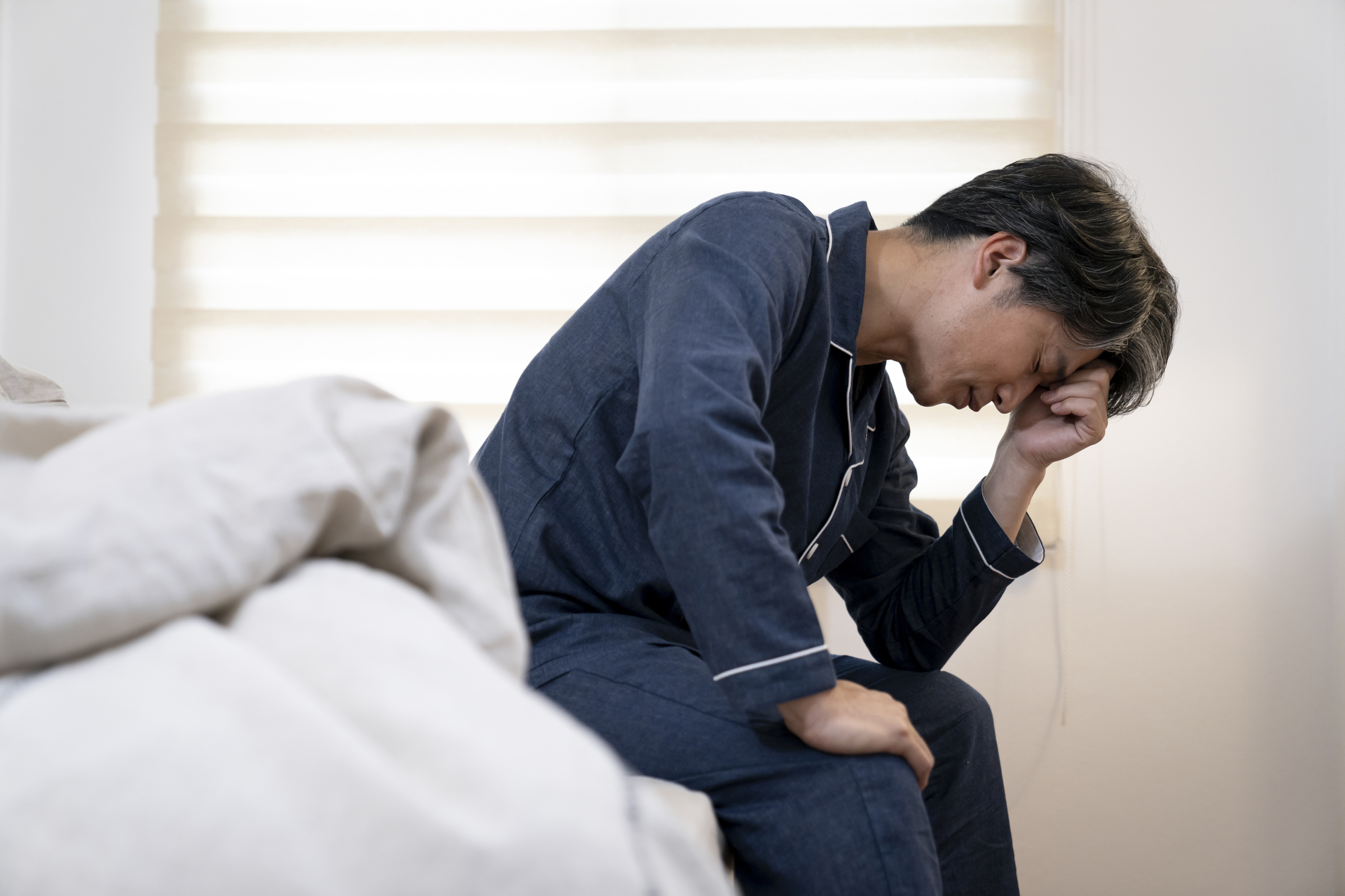 気分の落ち込みでベッドに座り込む男性（うつ状態のイメージ）│堺そらはねメンタルクリニック