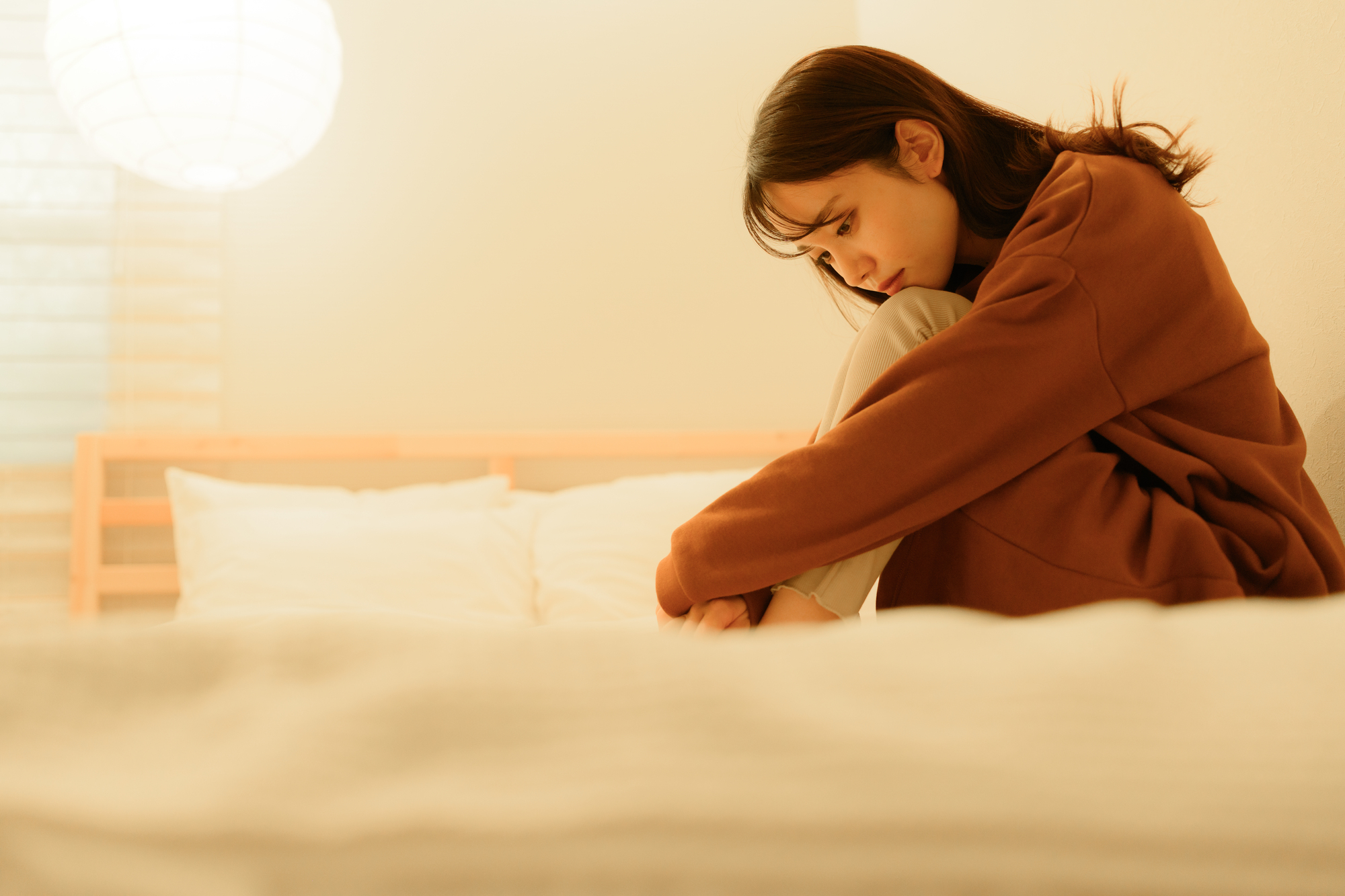 気分の波に悩む女性がベッドでうつむく様子│堺そらはねメンタルクリニック
